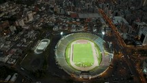 Aerial birds eye shot of illuminated soccer stadium surrounded by Quito Cityscape in Ecuador in the evening	