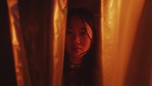 Portrait of Mysterious Asian Beauty among Cellophane Curtains in Neon Light
