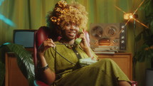 Young pretty Black woman with curly hair sitting in a studio with retro interior, smiling and chatting on old landline phone. Zoom Shot
