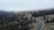Aerial shot of a highway on the sloping hills with conifer forest trees against a moody sky.