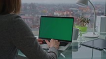 woman using laptop with green screen workspace in office with view of cityscape businesswoman working online
