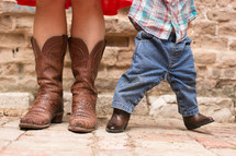 The feet of a woman and baby wearing cowboy boots