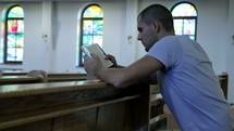 a man kneeling reading a Bible in a church 