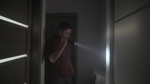 Man Walking And Looking Around Inside Dark House With Flashlight. medium shot	