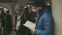 A man reading a Bible in a crowded subway station 