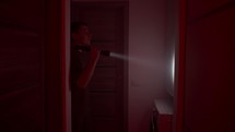 Man With Flashlight Looking Through The Dark House - Horror Concept.	