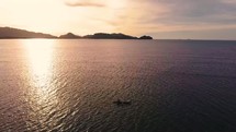 Slow drone pull back of a sunset in Papua New Guinea with man rowing canoe coming into the scene. 