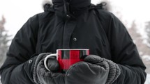 Person in black coat and gloves with a red mug with steam