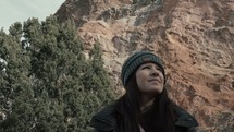 a woman in a coat and beanie looking around outdoors 
