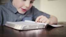 Child reading a Bible out loud to himself.