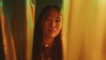 Portrait of Enigmatic Asian Woman behind Cellophane Curtains in Neon Light
