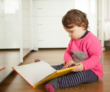 Toddler baby girl playing with fairy tales book on the oak wood floor.
