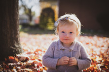 a shy little girl playing in fall leaves 