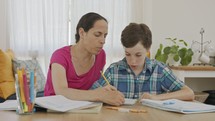 Mother helping her young son prepare homework during homeschooling