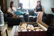box of donuts and people sitting on a couch 