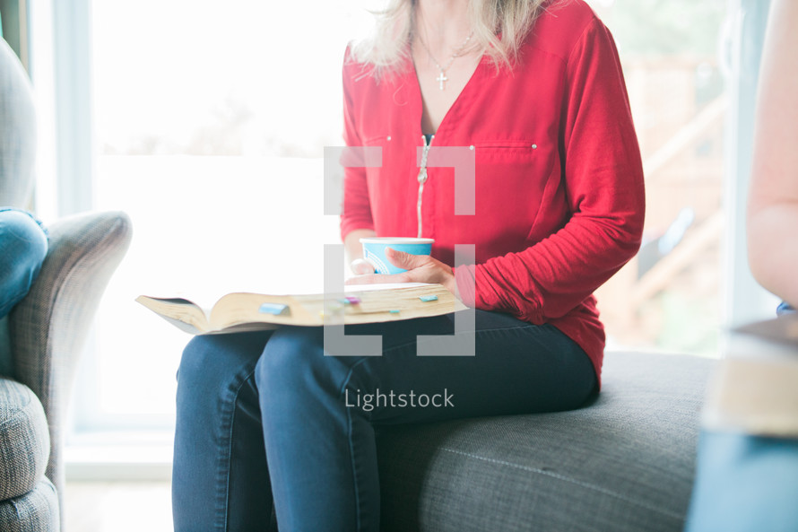 a woman sitting on a couch drinking coffee and reading a Bible 