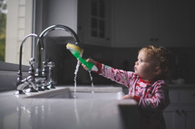 toddler girl playing with a sponge in a kitchen sink 
