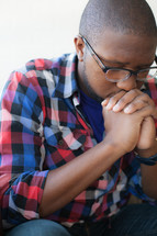 African-American man with glasses and praying hands and head bowed 