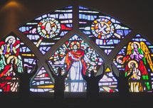 Silhouette of people with arms raised standing front of a stained glass window.