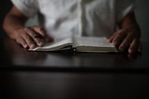 Hands holding a pen and the edges of an open Bible.