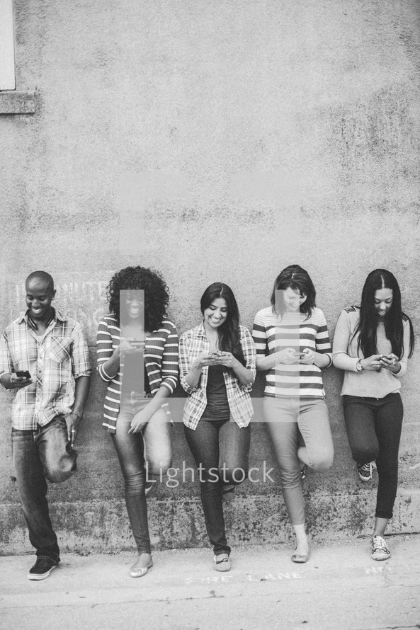 a row of young adults texting on their cellphones 