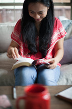 Asian woman reading a Bible on her couch 