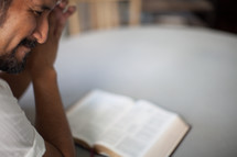 Man praying over an open bible on a table.