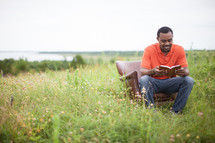 African-American, man sitting in a field reading a Bible 