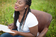 woman sitting in a chair outdoors reading a Bible smiling 