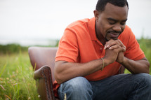 African-American man sitting in a chair outdoors in prayer 