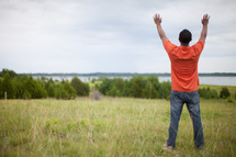 man standing in a field with hands raised to God 