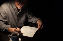 man writing in a journal and a coffee mug 