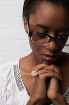face of an African-American woman with reading glasses and praying hands 