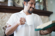 Smiling man holding a cup of coffee and and open Bible.
