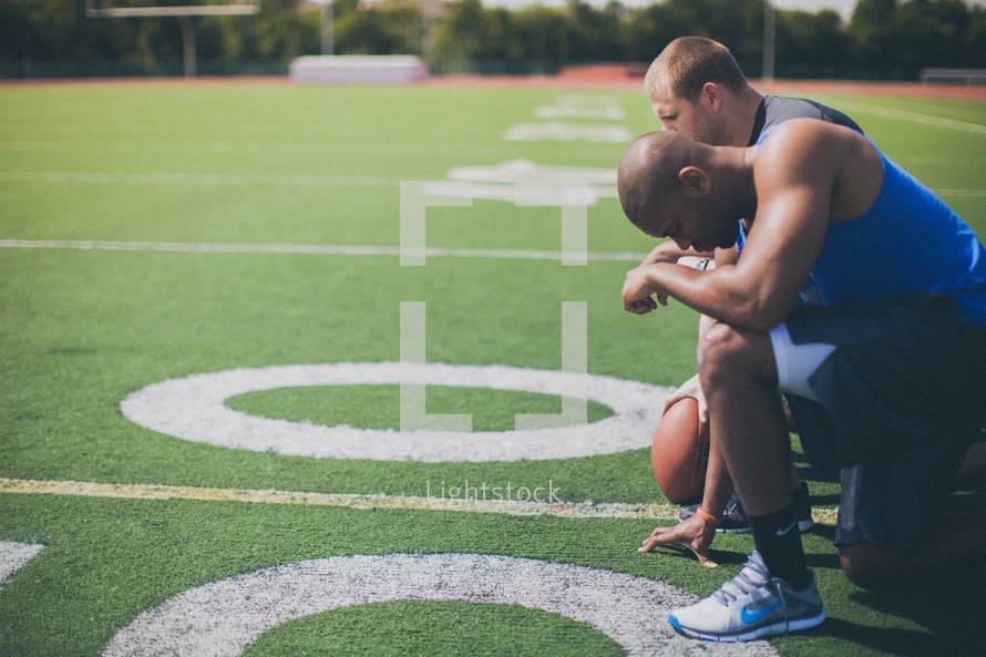 football players kneeling in prayer on the field