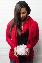 An African-American woman holding a wrapped Christmas gift with her head bowed in prayer 