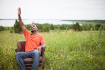 man sitting in a chair with hand raised to God outdoors 