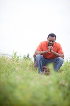 man sitting in a chair in a field with praying hands 
