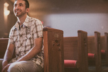 man sitting in a church pew smiling 