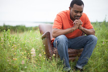 man sitting in a chair in a field outdoors in prayer 