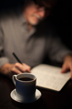 man writing in a journal and a coffee mug 