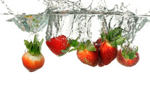 Strawberries submerged into water creating a splash.