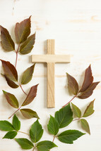 wooden cross with red and green leaves on a white wood background 