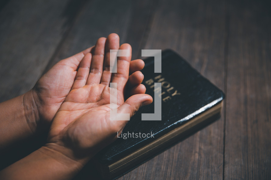 Hands open in prayer on a Bible