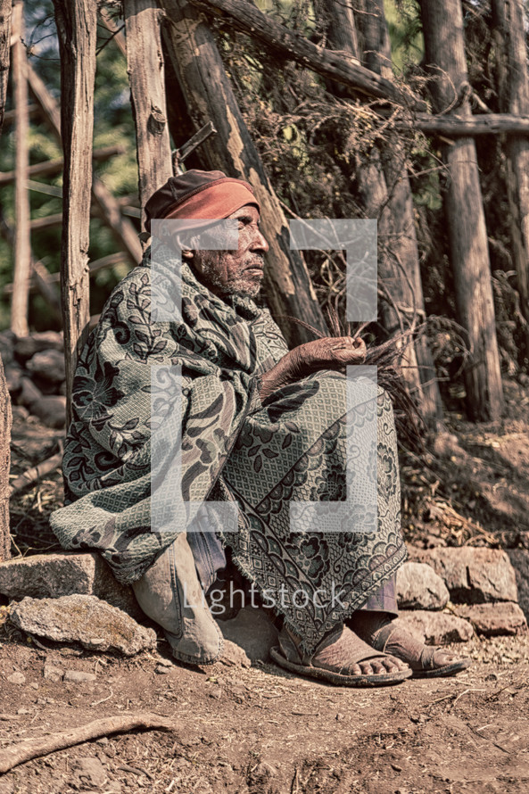 elderly man sitting on the ground wrapped in a blanket in Ethiopia 