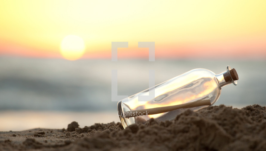 Message in a glass bottle on a beach with sunrise in background