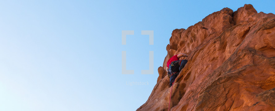 man climbing a red rock cliff with blue sky background for copy space