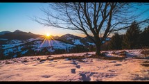 Timelapse of sunset view under cherry tree in winter alpine snowy nature on cold evening .
