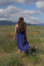 A woman in a blue dress walks through a field.