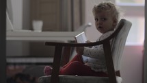 A baby girl sitting in a chair with a tablet on her laps